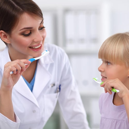 Dentist holding a toothbrush demonstrating how to brush teeth to a young child