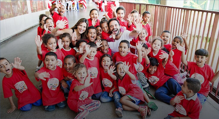group of children wearing red t-shirts smiling and waving