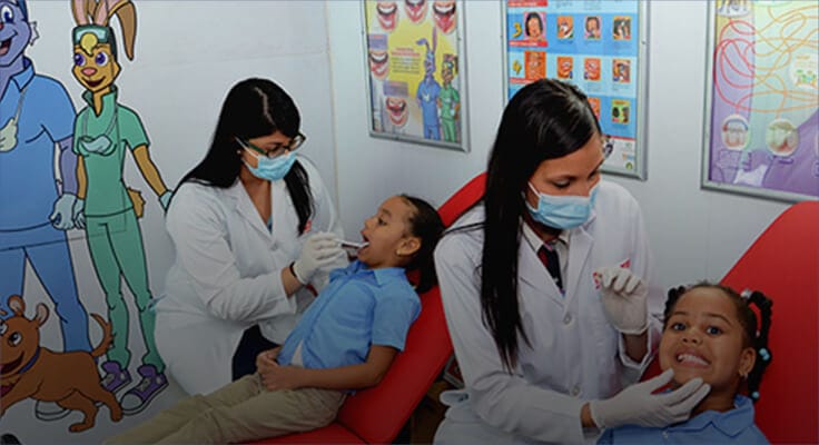Dental professional with mask and gloves on inspecting a child mouth