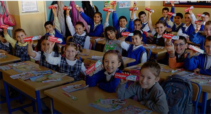 children smiling and holding a Colgate toothpaste box in a classroom