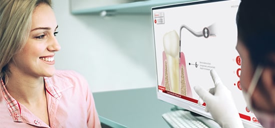 Dental professional pointing at a screen showing a patient wearing a pink shirt 