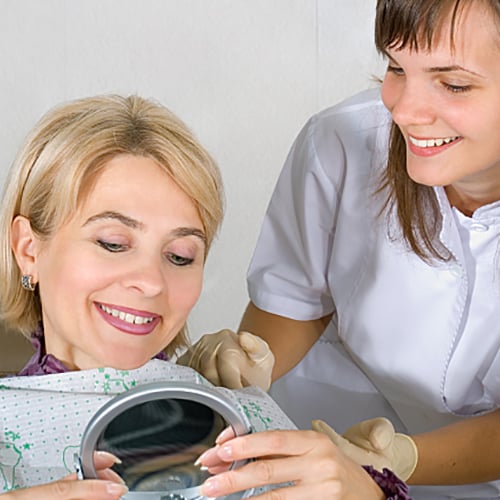 Patient looking at herself in the handheld mirror while the dentist looks over her shoulder 