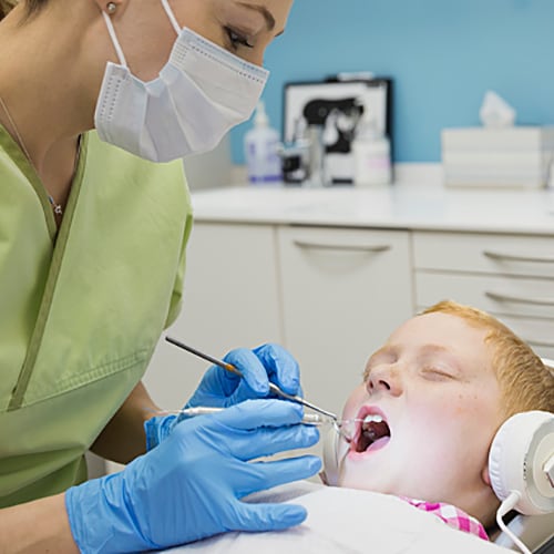 Child with mouth open getting treatment from nurse wearing a green scrub