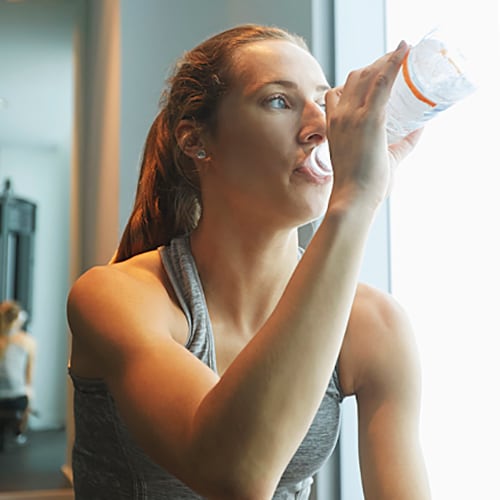 Woman wearing work-out gear drinking water in a gym 