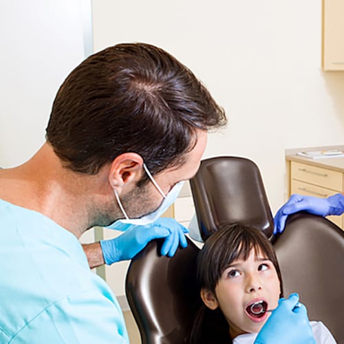 Two dental professionals looking into a child's mouth as she sits in the dental chair
