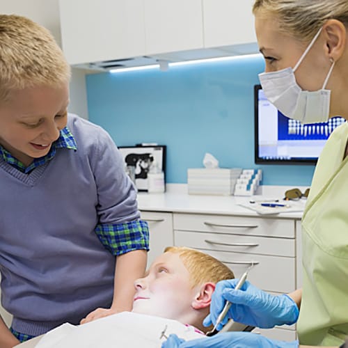 Dentil Hygienist and two children in the treatment room while one child is on the dental chair 