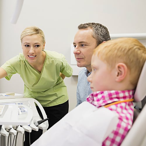 Nurse in green scrubs explaining x-rays to father and son duo in a treatment room