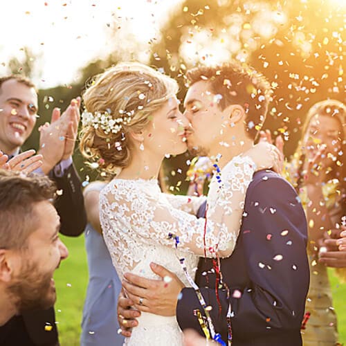 Recently married couple kissing in the middle of their wedding guests with confetti in the air