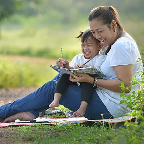 Mother and toddler laughing as they are sitting and coloring a color book outside