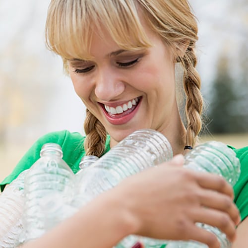 Girl in green shirt smiling while holding plastic water bottles 