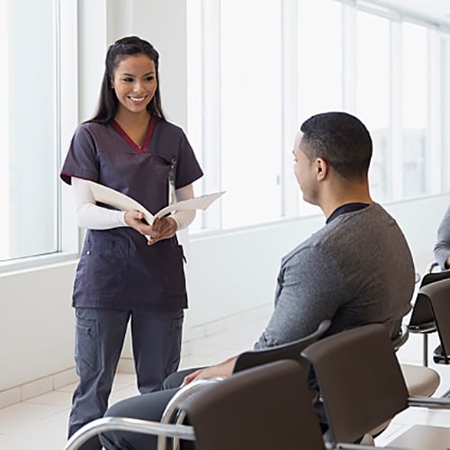Nurse talking to patient in the waiting room while other patient is in the background reading