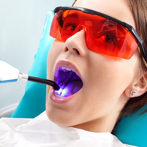 There's a laser machine inside of a woman’s mouth and she's wearing red glasses