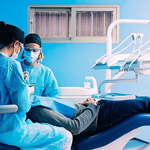Two dental hygienists assisting a patient in a treatment room
