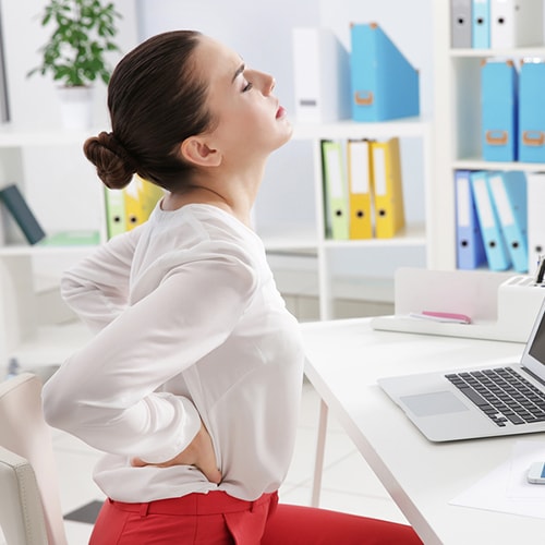 The woman arches her back as she holds her waist with her hands in front of a laptop 