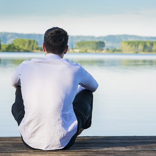 man sitting cross-legged in front of lake