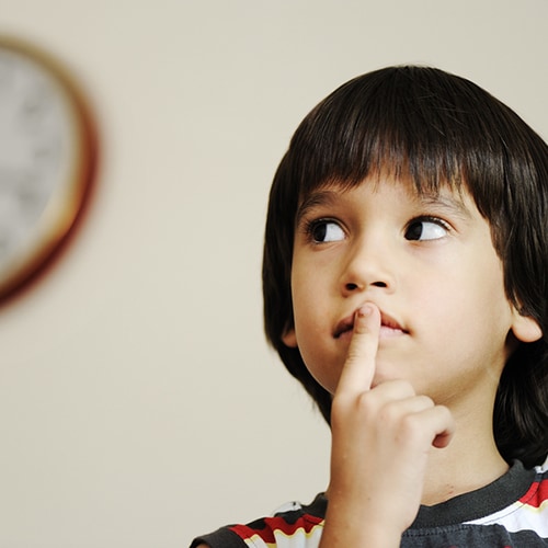 Young child putting index finger over mouth and there's a clock in the background