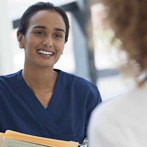 Nurse in blue scrubs smiling while looking directly at doctor 