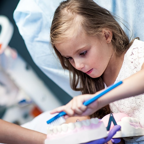 Nurse watching a young girl using a tooth brush on a teeth model 