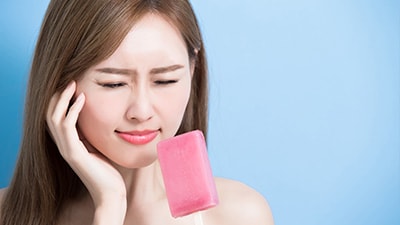 woman squinting in pain while holding an ice popsicle