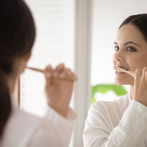 young woman in bathrobe brushing her teeth with wooden toothbrush