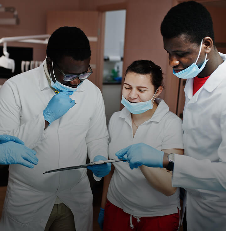 Team of 3 dental professionals wearing white coats, looking at a patient chart